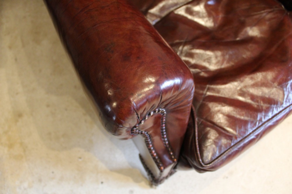 A late Victorian deep-buttoned chestnut brown leather wingback armchair featuring brass studding, carved front legs with ball-and-claw feet, and metal castors. View VI