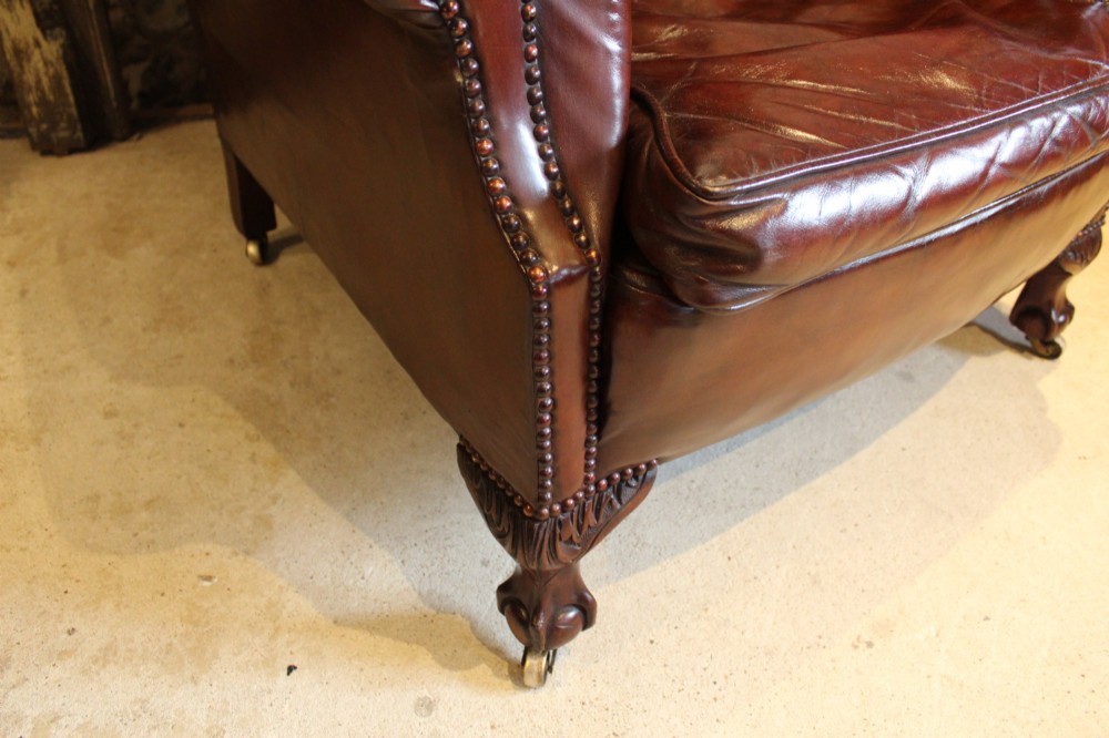 A late Victorian deep-buttoned chestnut brown leather wingback armchair featuring brass studding, carved front legs with ball-and-claw feet, and metal castors. View IX