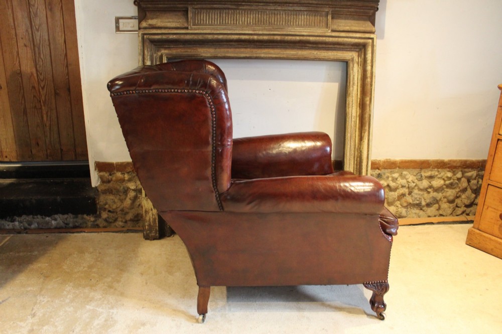 A late Victorian deep-buttoned chestnut brown leather wingback armchair featuring brass studding, carved front legs with ball-and-claw feet, and metal castors. View X