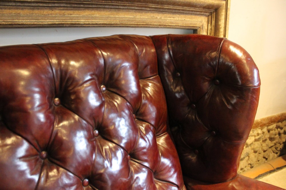 A late Victorian deep-buttoned chestnut brown leather wingback armchair featuring brass studding, carved front legs with ball-and-claw feet, and metal castors. View XI