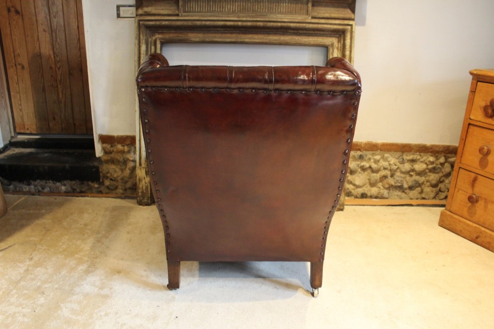 A late Victorian deep-buttoned chestnut brown leather wingback armchair featuring brass studding, carved front legs with ball-and-claw feet, and metal castors. View XII