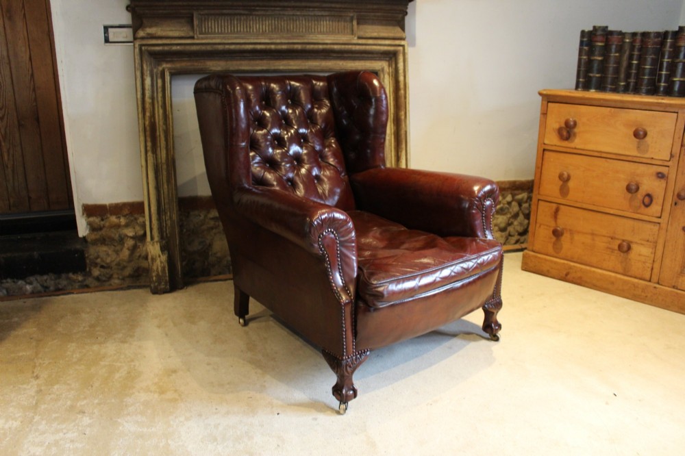 A late Victorian deep-buttoned chestnut brown leather wingback armchair featuring brass studding, carved front legs with ball-and-claw feet, and metal castors. View XIII