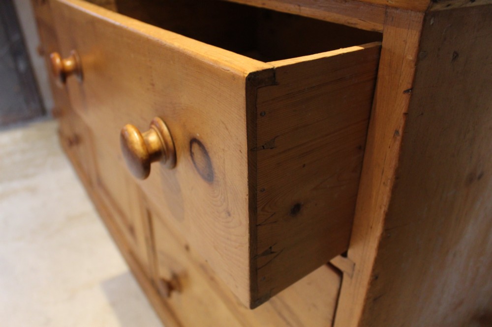 An early Victorian honey pine dresser base featuring a central panelled cupboard door flanked by three drawers on each side with turned wooden knobs. View IV