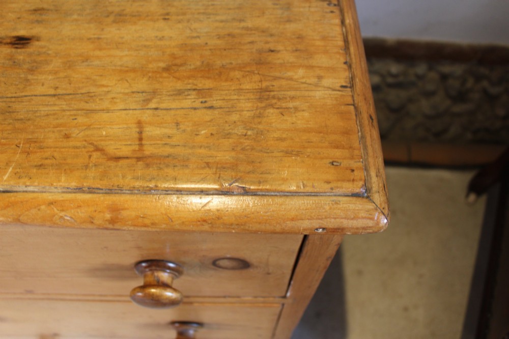 An early Victorian honey pine dresser base featuring a central panelled cupboard door flanked by three drawers on each side with turned wooden knobs. View VI