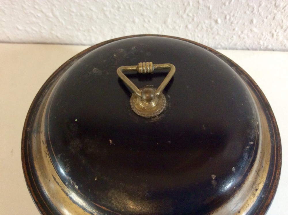 A circular black toleware spice box featuring a domed lid, brass top ring handle, gold accent band, and front metal latch. View V