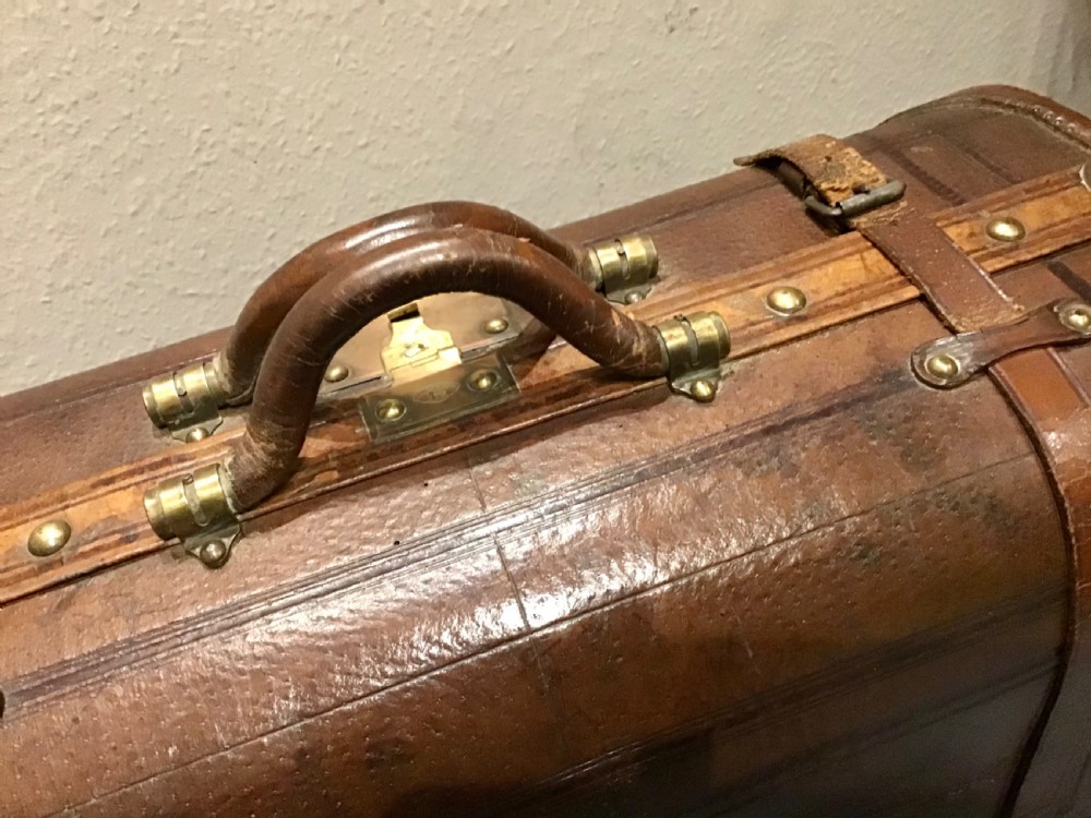 An antique dark brown leather valise suitcase featuring brass hardware, stitched straps, and embossed geometric detailing. View II