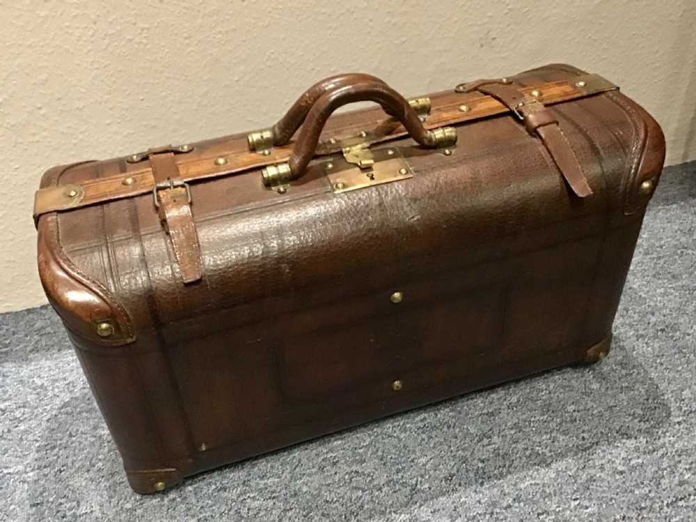 An antique dark brown leather valise suitcase featuring brass hardware, stitched straps, and embossed geometric detailing. View III