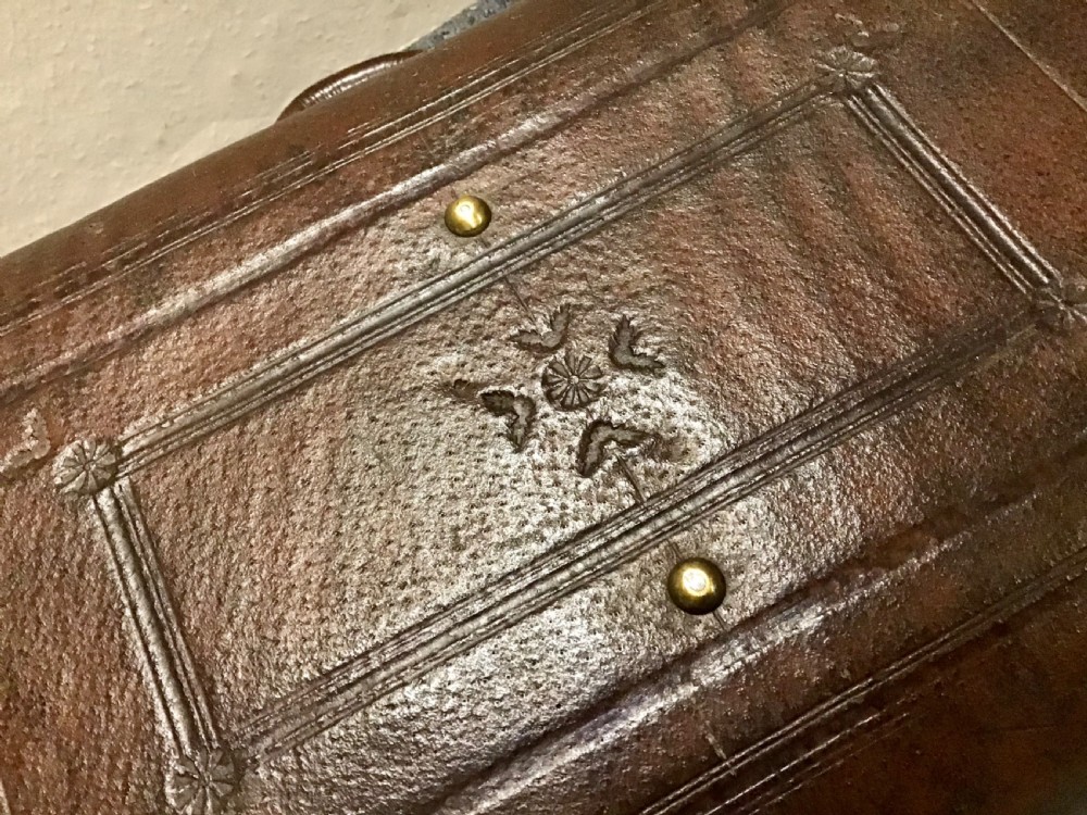 An antique dark brown leather valise suitcase featuring brass hardware, stitched straps, and embossed geometric detailing. View VII