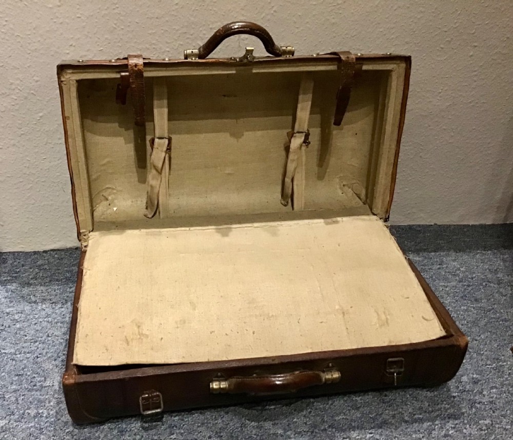 An antique dark brown leather valise suitcase featuring brass hardware, stitched straps, and embossed geometric detailing. View X