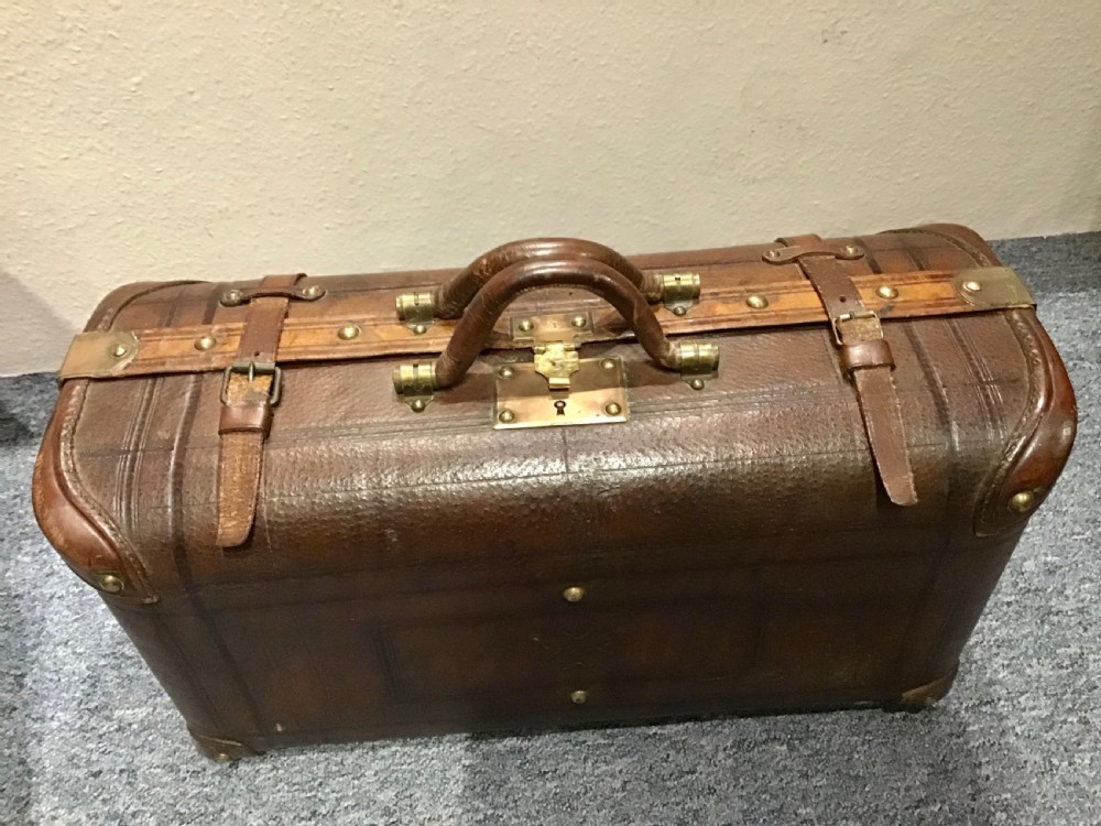 An antique dark brown leather valise suitcase featuring brass hardware, stitched straps, and embossed geometric detailing. View XII