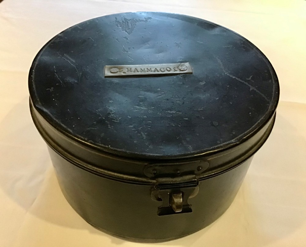 A circular dark metal naval cap box with a hinged lid, front latch, and a riveted nameplate on top reading S. Hammacott.