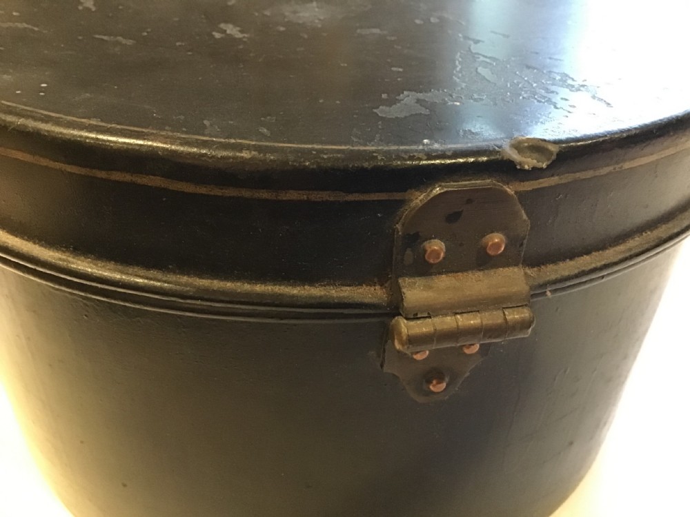 A circular dark metal naval cap box with a hinged lid, front latch, and a riveted nameplate on top reading S. Hammacott. View VII