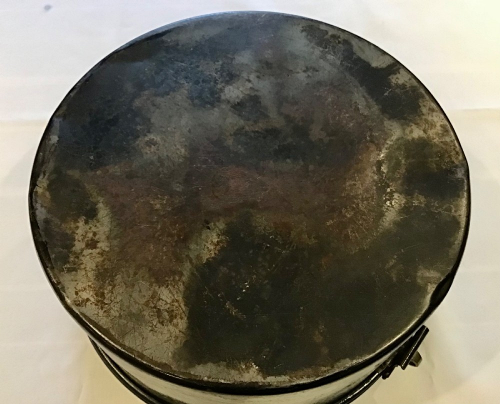 A circular dark metal naval cap box with a hinged lid, front latch, and a riveted nameplate on top reading S. Hammacott. View IX