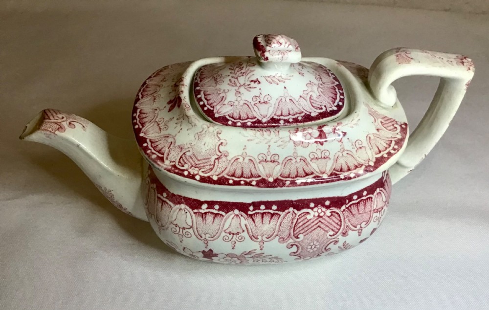 A small Victorian earthenware teapot with a lid, featuring red transferware floral and swag patterns against a cream background.