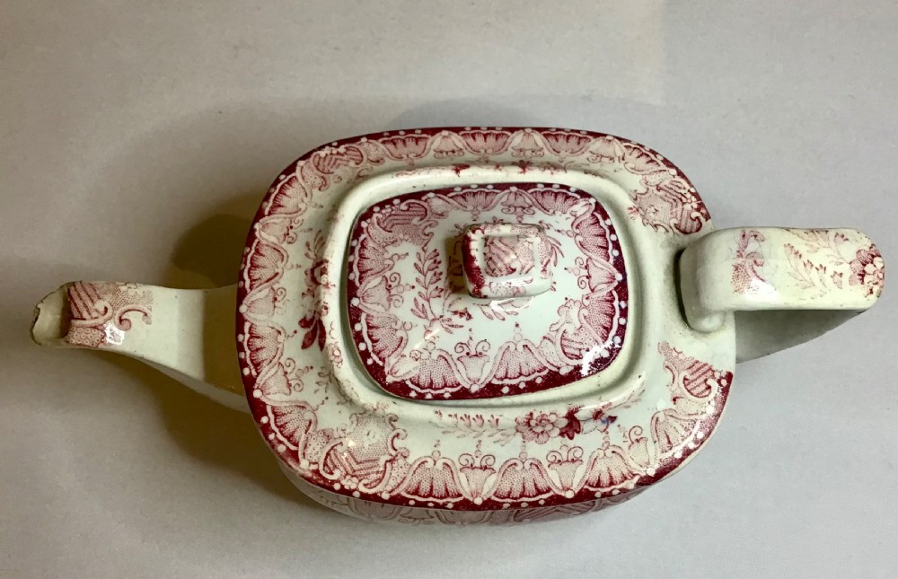 A small Victorian earthenware teapot with a lid, featuring red transferware floral and swag patterns against a cream background. View VI