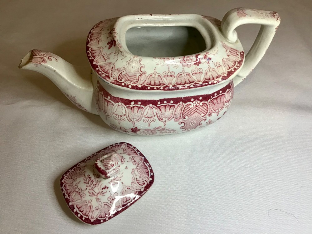 A small Victorian earthenware teapot with a lid, featuring red transferware floral and swag patterns against a cream background. View VII