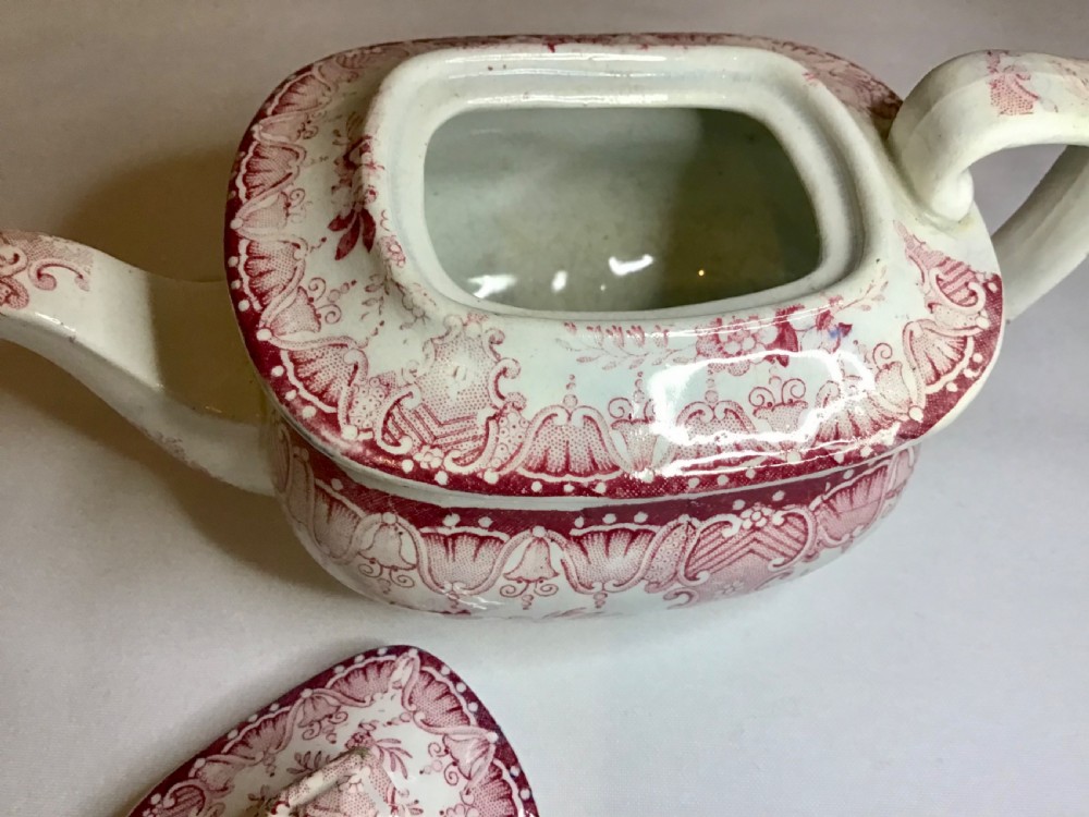 A small Victorian earthenware teapot with a lid, featuring red transferware floral and swag patterns against a cream background. View VIII