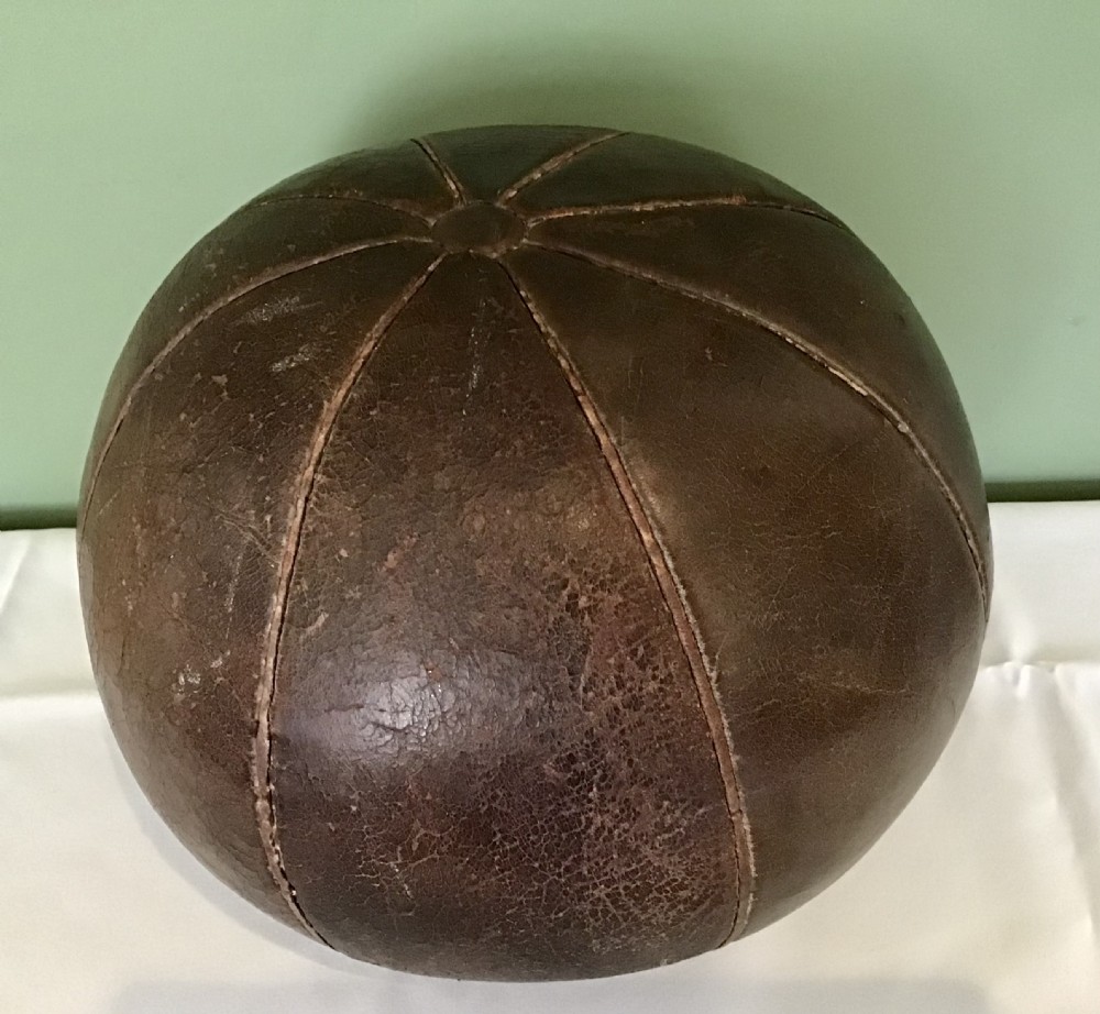 A spherical Edwardian medicine ball crafted from dark brown stitched leather panels displaying a weathered patina.