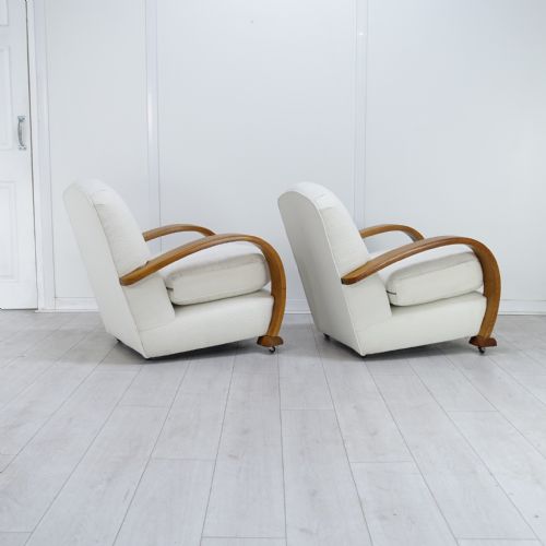 fig 1. A pair of 1930s Art Deco armchairs upholstered in cream textured fabric featuring sweeping bentwood wooden armrests and castors.