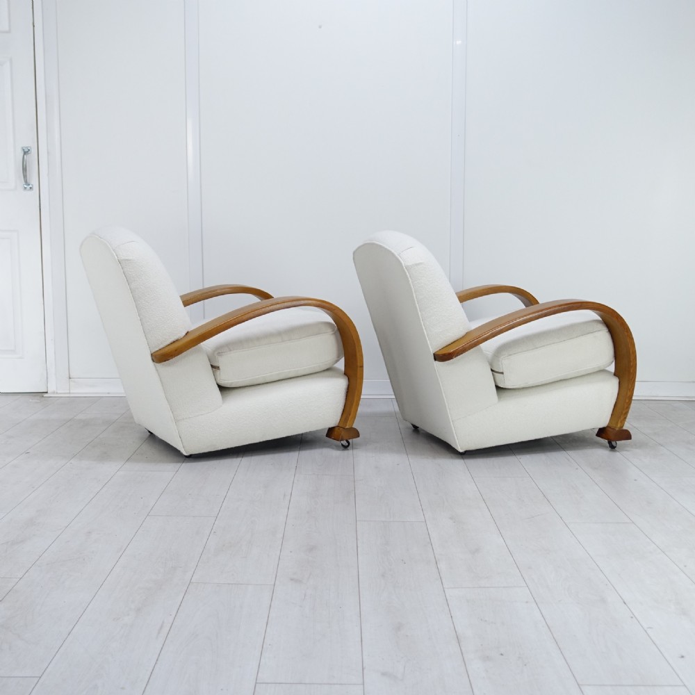 A pair of 1930s Art Deco armchairs upholstered in cream textured fabric featuring sweeping bentwood wooden armrests and castors. View II