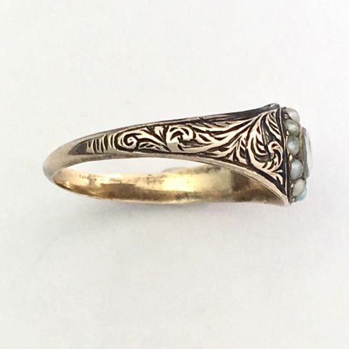 fig 2. A Georgian 9ct gold mourning ring featuring a central oval glass compartment containing hair surrounded by a halo of seed pearls and scroll-engraved shoulders.