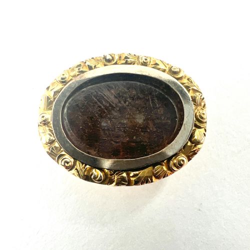 fig 1. An oval Georgian gold brooch with a chased scroll border surrounding a glass compartment containing brown woven hair.