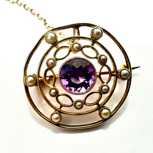 fig 1. An Edwardian 9ct yellow gold circular target brooch featuring a central round purple amethyst surrounded by openwork concentric rings set with seed pearls, attached to a safety chain.