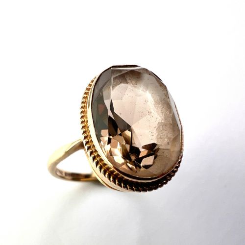 fig 1. A vintage yellow gold ring set with a large oval faceted translucent brown smoky quartz stone framed by a twisted rope bezel detail.