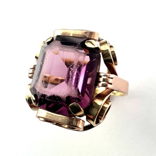 fig 1. A 1940s Retro 14ct gold cocktail ring featuring a large rectangular cut purple paste gemstone set within ornate metal scrollwork.