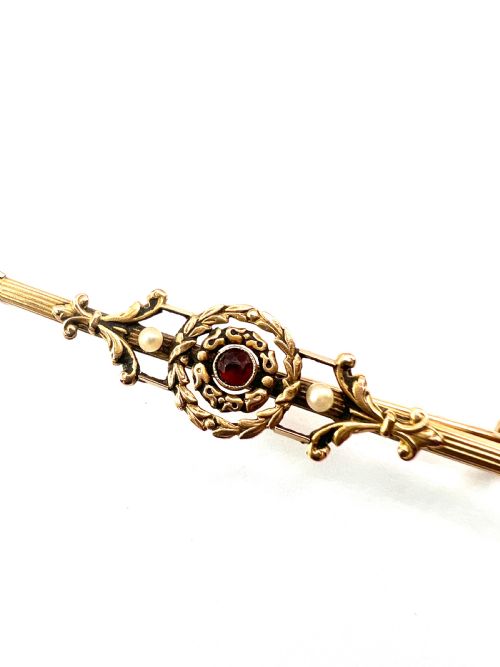fig 1. An antique 18-carat yellow gold bar brooch featuring a central circular motif with a round red garnet flanked by seed pearls and fluted bar details.