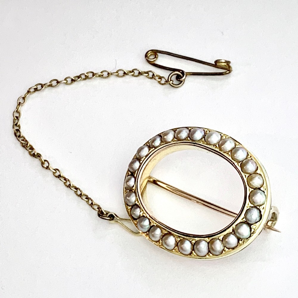 An oval 9ct gold Victorian halo brooch set with a border of seed pearls, featuring an attached safety chain.