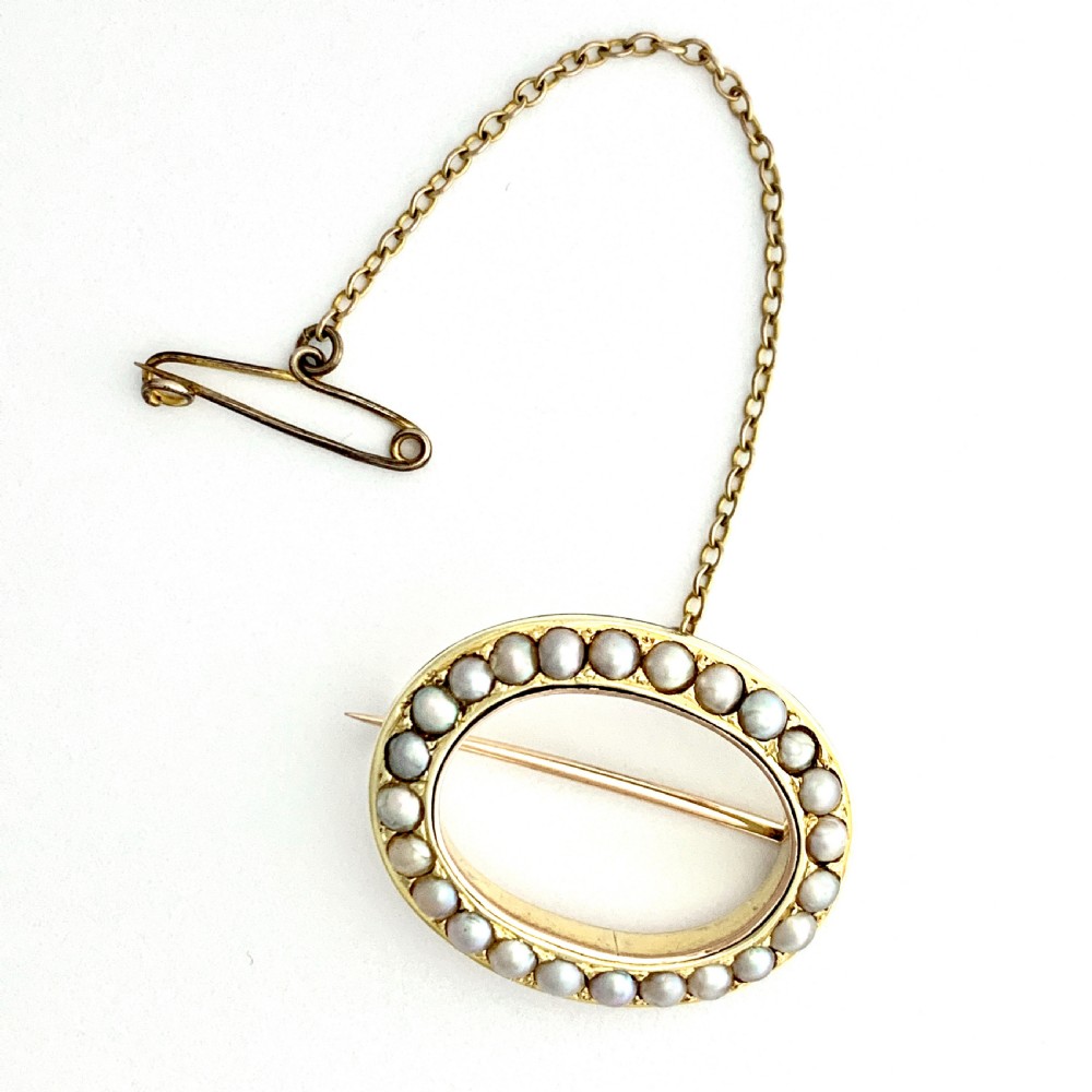 An oval 9ct gold Victorian halo brooch set with a border of seed pearls, featuring an attached safety chain. View II