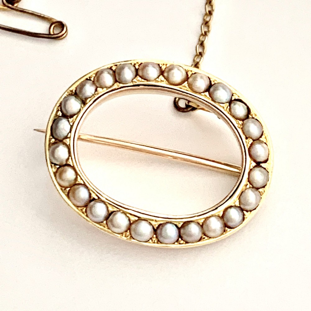 An oval 9ct gold Victorian halo brooch set with a border of seed pearls, featuring an attached safety chain. View III