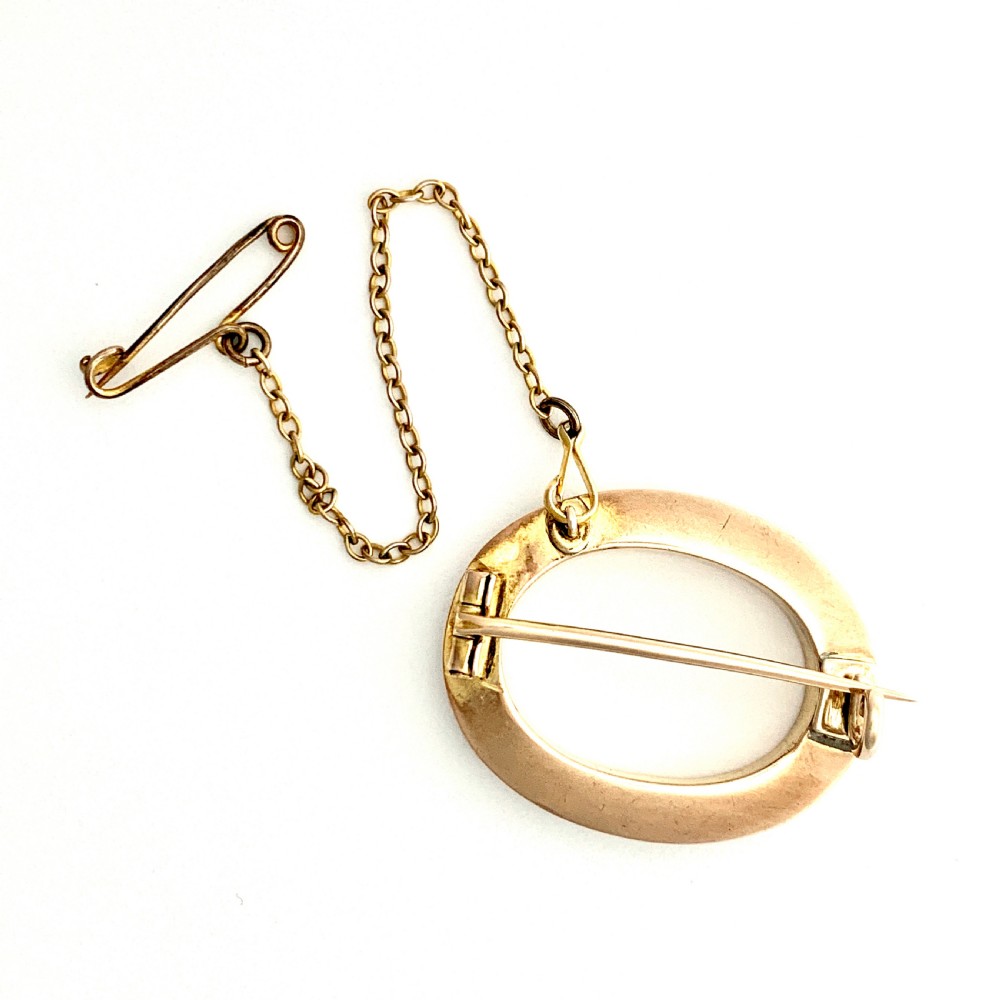 An oval 9ct gold Victorian halo brooch set with a border of seed pearls, featuring an attached safety chain. View IV