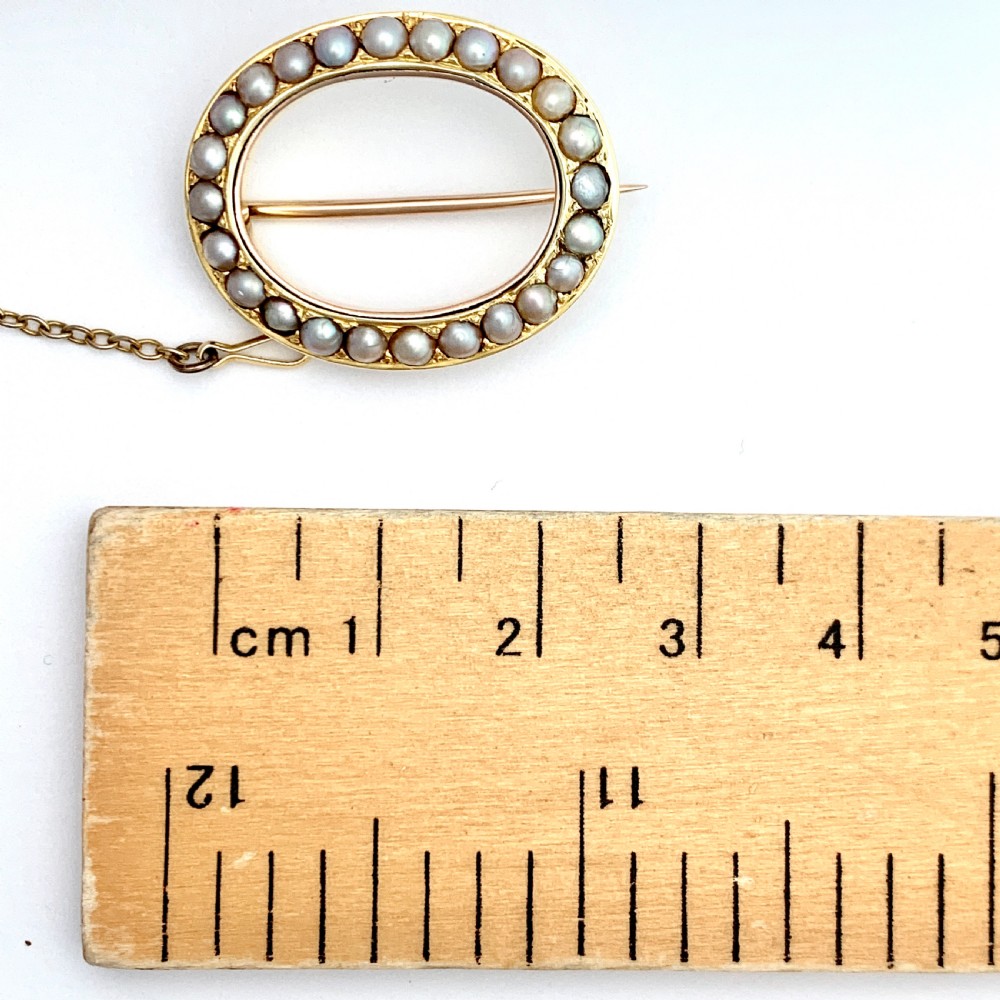 An oval 9ct gold Victorian halo brooch set with a border of seed pearls, featuring an attached safety chain. View V
