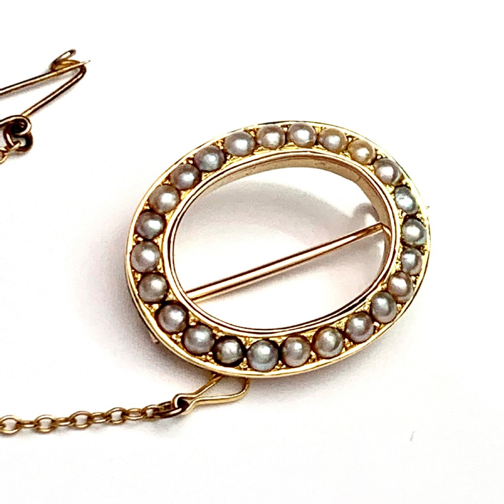 An oval 9ct gold Victorian halo brooch set with a border of seed pearls, featuring an attached safety chain. View VI