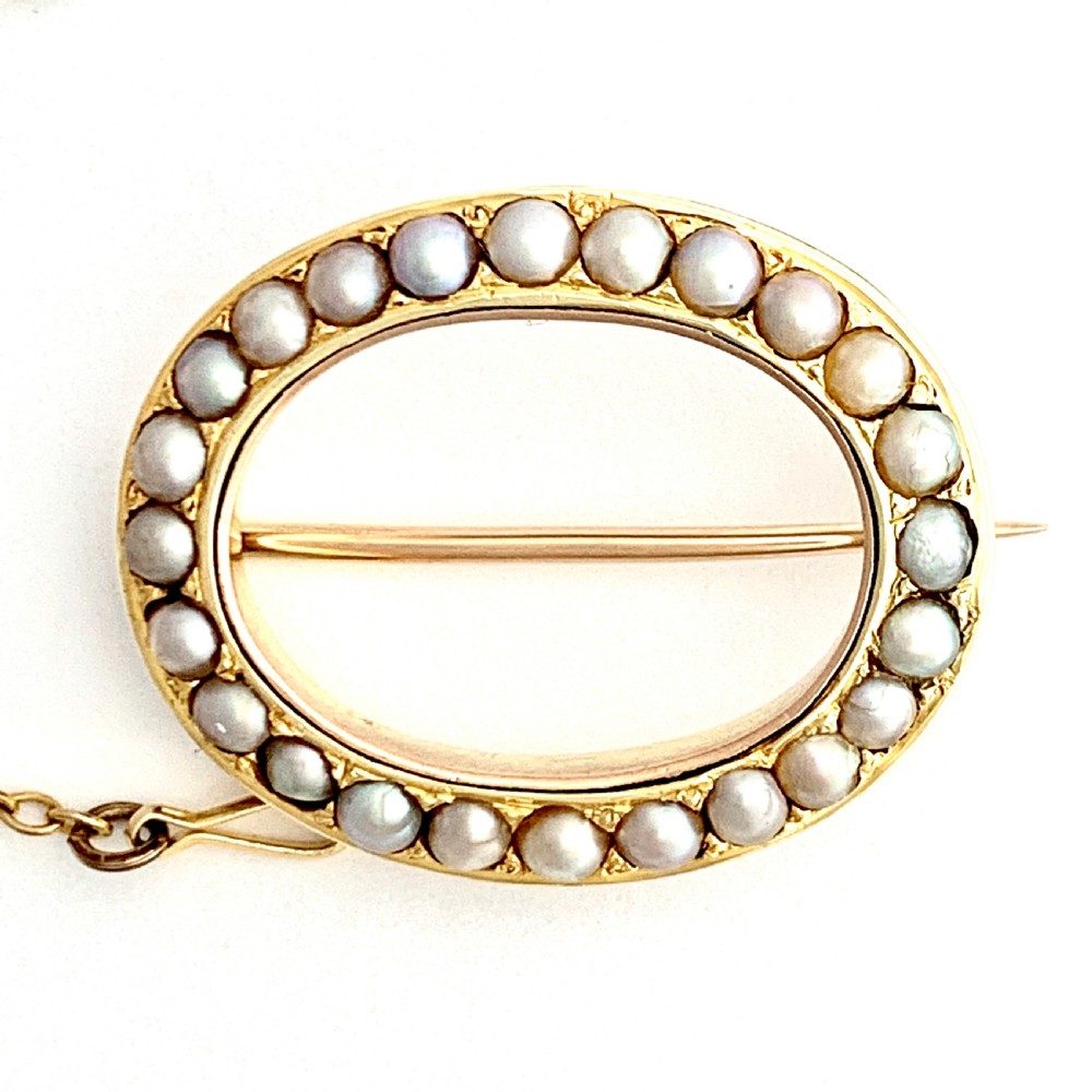 An oval 9ct gold Victorian halo brooch set with a border of seed pearls, featuring an attached safety chain. View VII