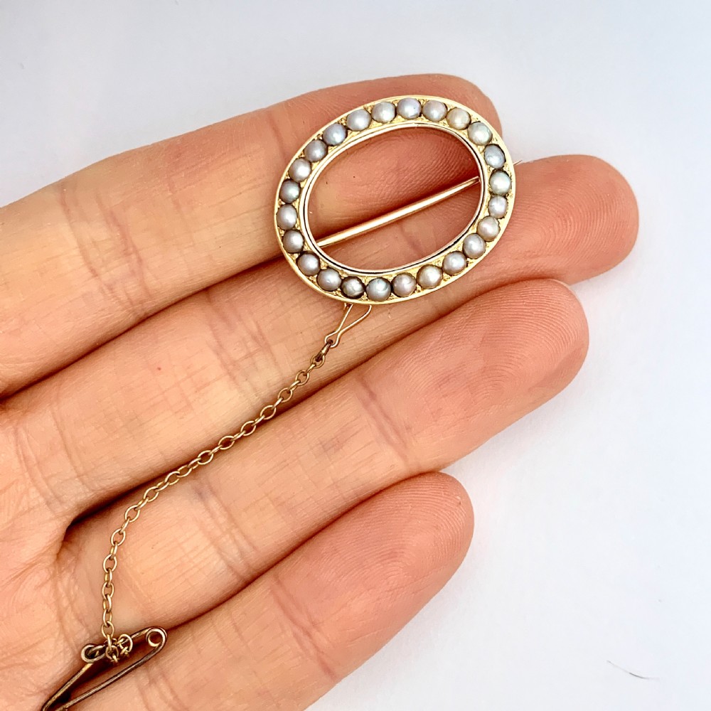 An oval 9ct gold Victorian halo brooch set with a border of seed pearls, featuring an attached safety chain. View VIII
