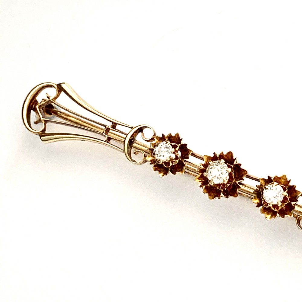 An Edwardian 14ct yellow gold bar brooch featuring three starburst-set diamonds along a openwork frame.