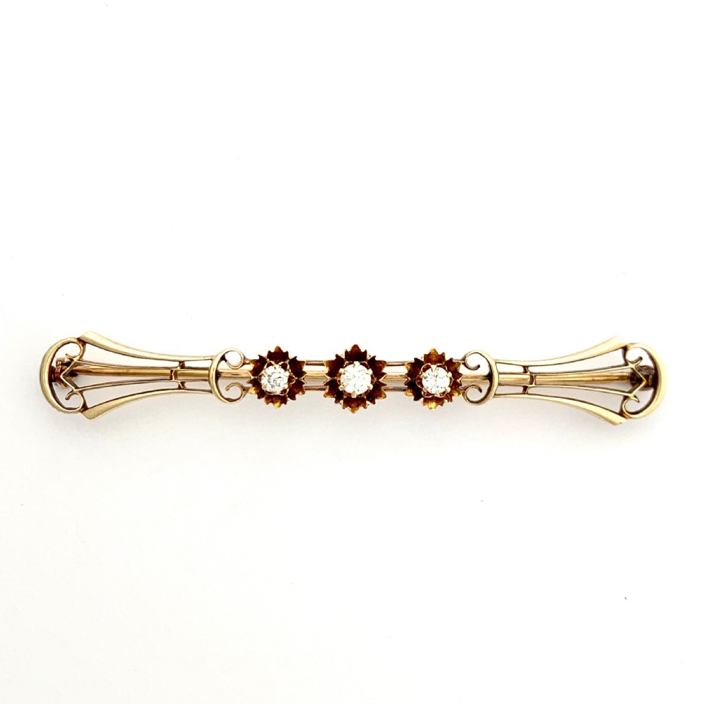 An Edwardian 14ct yellow gold bar brooch featuring three starburst-set diamonds along a openwork frame. View V