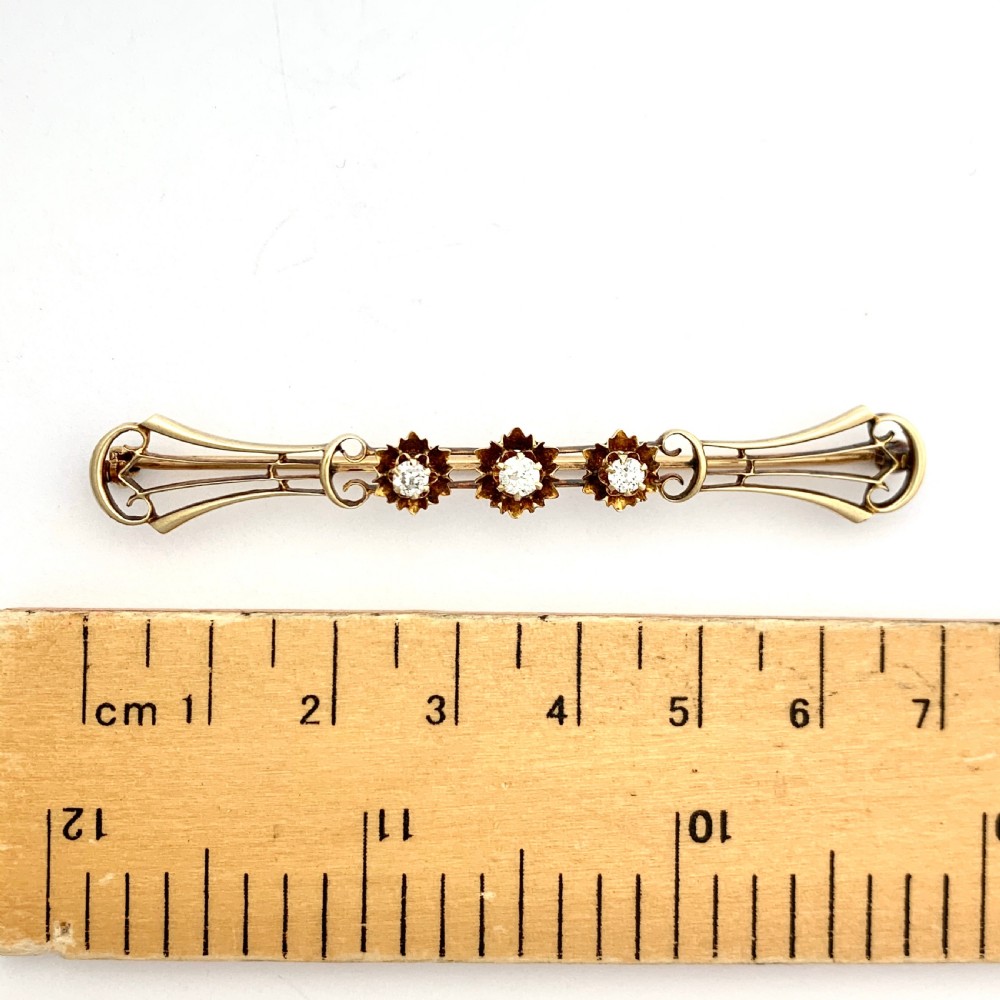 An Edwardian 14ct yellow gold bar brooch featuring three starburst-set diamonds along a openwork frame. View VI