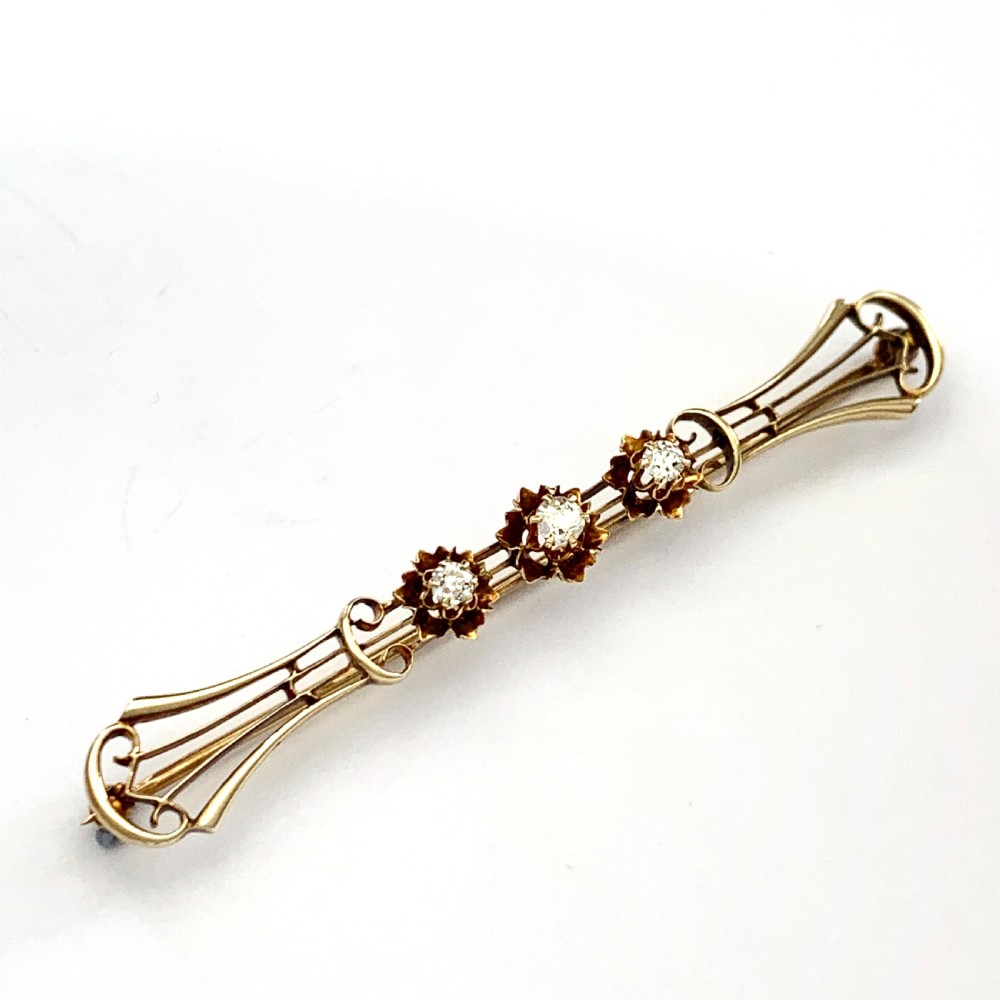 An Edwardian 14ct yellow gold bar brooch featuring three starburst-set diamonds along a openwork frame. View VII