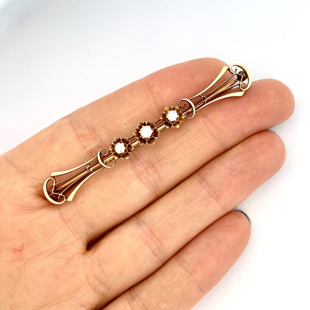 An Edwardian 14ct yellow gold bar brooch featuring three starburst-set diamonds along a openwork frame. View VIII