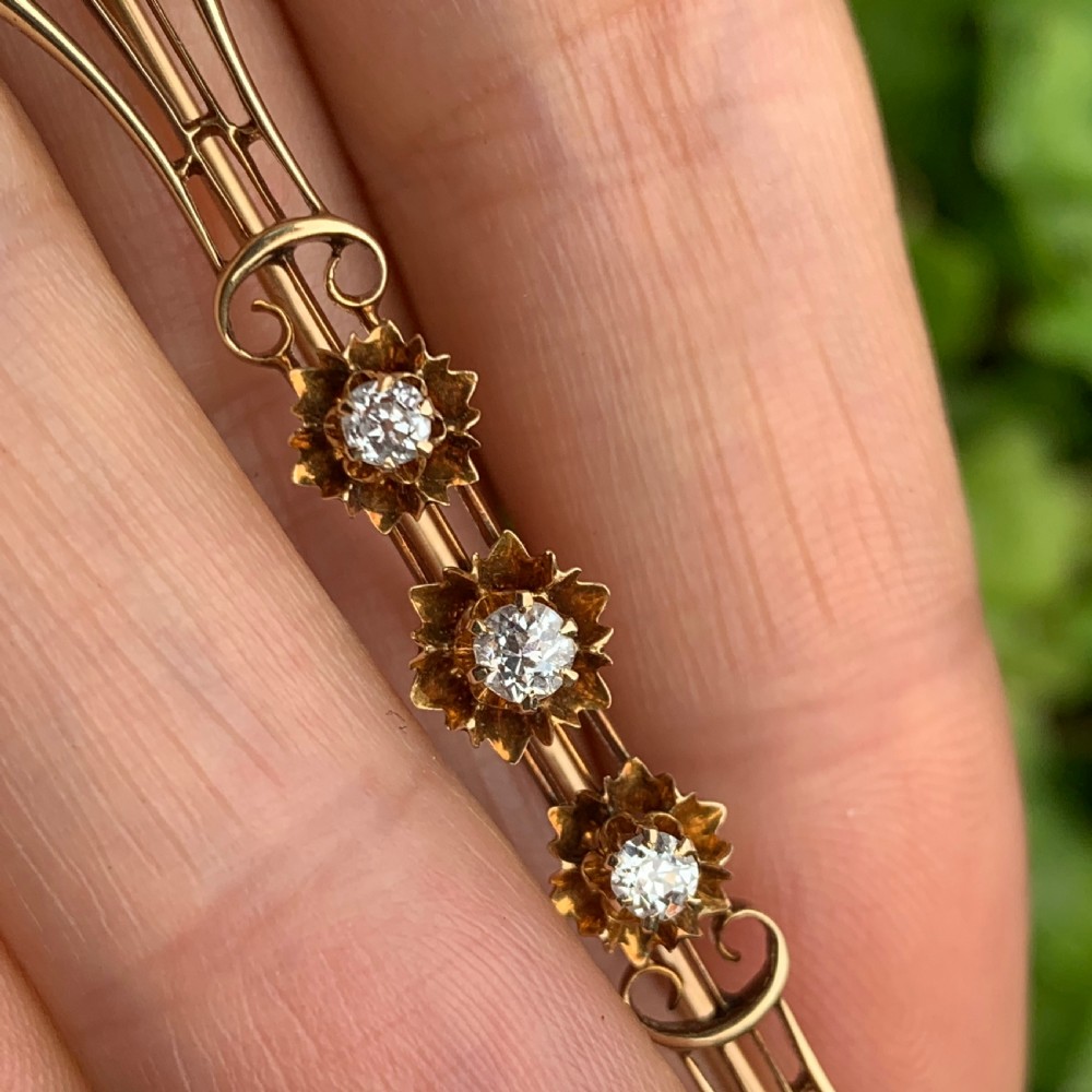 An Edwardian 14ct yellow gold bar brooch featuring three starburst-set diamonds along a openwork frame. View IX
