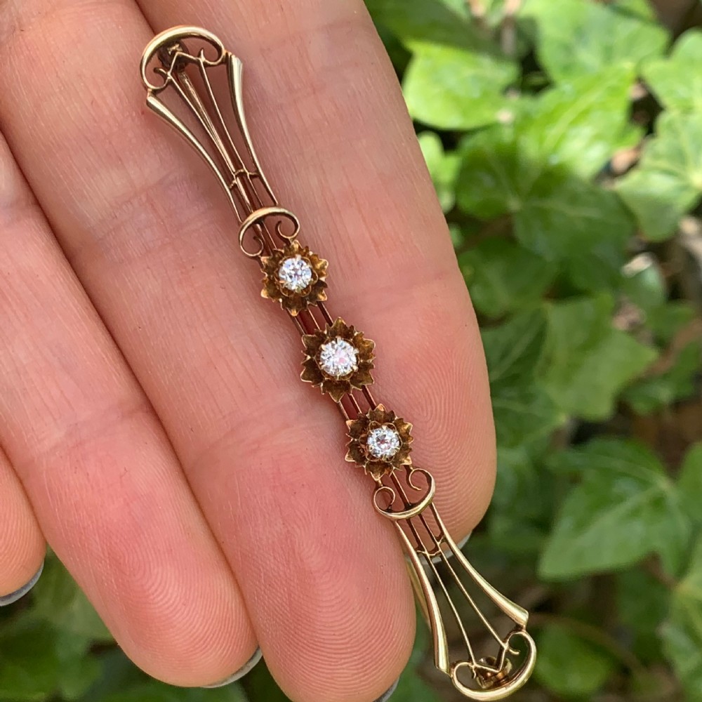 An Edwardian 14ct yellow gold bar brooch featuring three starburst-set diamonds along a openwork frame. View X