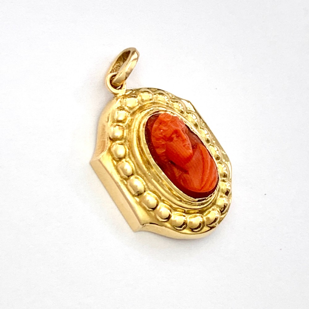 An oval Victorian 18ct gold pendant featuring an orange-red carved coral cameo classical bust framed by a beaded gold border. View VI