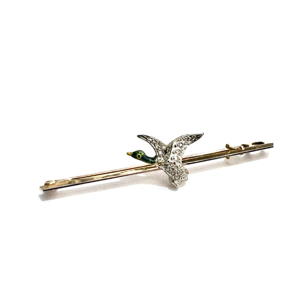 An Edwardian 15ct gold bar brooch featuring a flying duck set with diamonds and green enamel details.