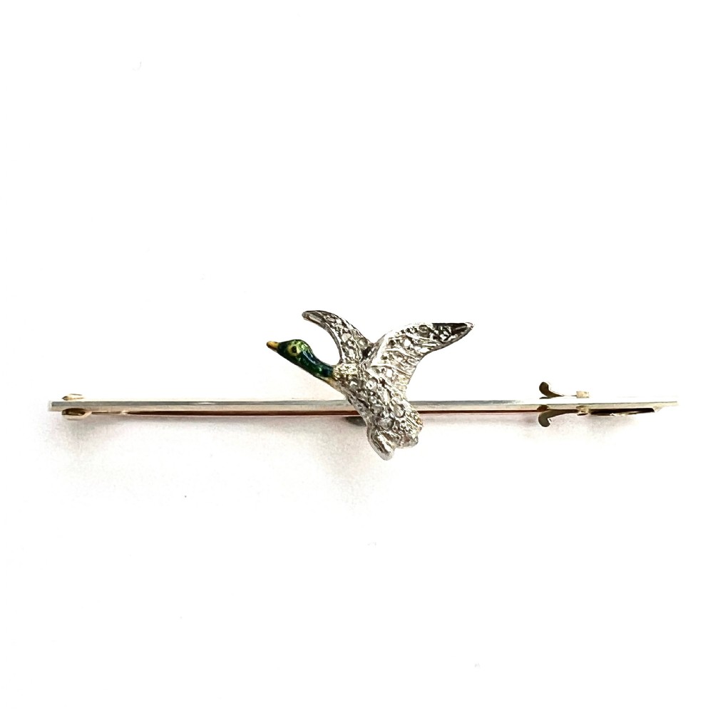 An Edwardian 15ct gold bar brooch featuring a flying duck set with diamonds and green enamel details. View IV