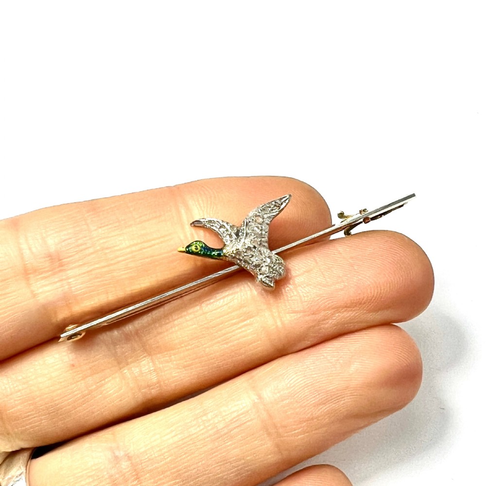 An Edwardian 15ct gold bar brooch featuring a flying duck set with diamonds and green enamel details. View VI