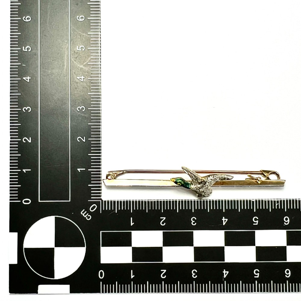 An Edwardian 15ct gold bar brooch featuring a flying duck set with diamonds and green enamel details. View VII